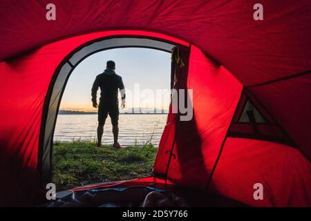 Homme campant en Estonie, debout devant la tente, regardant le coucher du soleil Banque D'Images