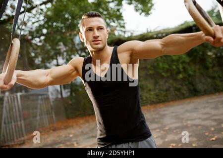 Jeune homme musclé de la formation sur les anneaux de gymnastique Banque D'Images