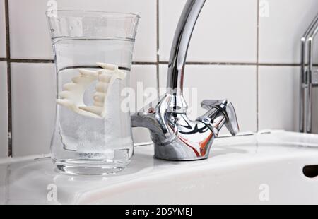 Dentiers vampire en verre d'eau sur lavabo de salle de bains Banque D'Images