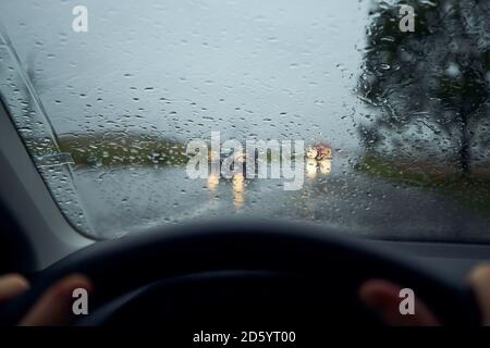 Conduite par forte pluie. Gouttes de pluie sur le pare-brise de la voiture contre la circulation au carrefour. Banque D'Images