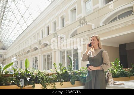 Une jeune femme parle sur son téléphone portable tout en étant debout dans le bâtiment à l'architecture magnifique Banque D'Images