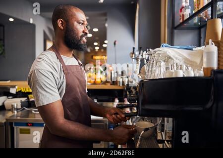 Un beau barman utilisant une machine à café professionnelle dans le café Banque D'Images