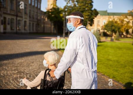 Personne médicale poussant un fauteuil roulant avec un citoyen âgé Banque D'Images