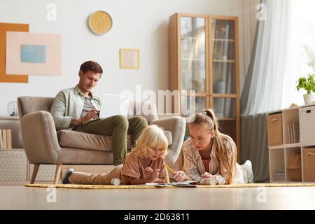 Mère avec son fils couché sur le sol et dessin pendant que leur père travaille sur un ordinateur portable assis sur un canapé, ils sont dans le salon Banque D'Images
