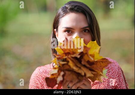 Portrait de la femme brune sur fond d'automne tenant des feuilles jaunes Banque D'Images