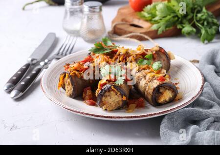 Petits pains d'aubergines cuits avec poulet, oignons et carottes dans une assiette sur fond gris. Gros plan. Banque D'Images