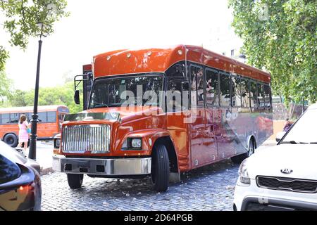 Un bus Freightliner orange garait dans le centre-ville de San Juan, avec un bus à l'arrière-plan et une voiture garée à côté. Banque D'Images