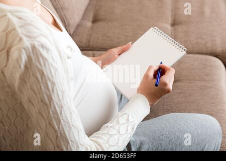 La femme enceinte prend des notes. Concept de grossesse, soins de santé, médecine. Mère attendant de bébé à la maison. Banque D'Images