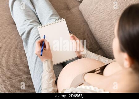 La femme enceinte prend des notes. Concept de grossesse, soins de santé, médecine. Mère attendant de bébé à la maison. Banque D'Images