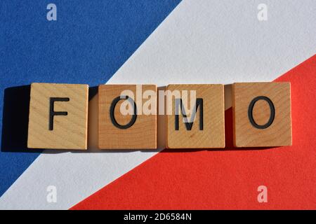 FOMO acronyme de Fear of Missing Out en lettres de l'alphabet en bois sur fond rouge, blanc et bleu Banque D'Images