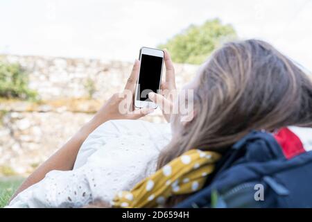 Une image de maquette de jeunes femmes méconnues tenant des mains blanches téléphone portable avec écran noir vierge maintenu entre les mains tout en étant couché et en refroidissant dans le Banque D'Images