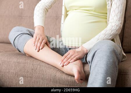 Crampes aux jambes pendant la grossesse. Gros plan des mains massant le pied gonflé tout en étant assis sur le canapé. Banque D'Images
