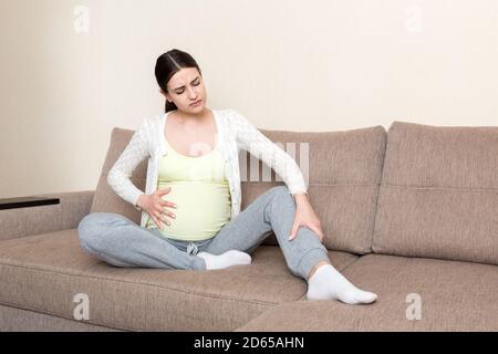 Crampes aux jambes pendant la grossesse. Gros plan des mains massant le pied gonflé tout en étant assis sur le canapé. Banque D'Images