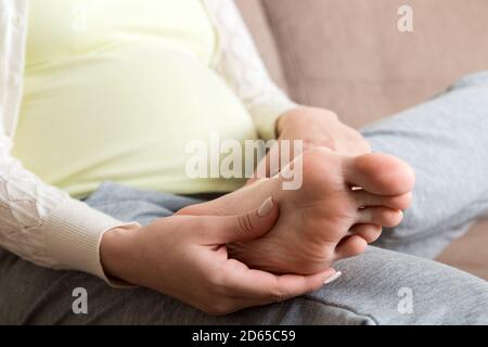 Crampes aux jambes pendant la grossesse. Gros plan des mains massant le pied gonflé tout en étant assis sur le canapé. Banque D'Images
