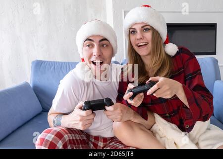 Jeu vidéo, loisirs et vacances concept. Homme et femme s'amusant avec la console de jeux vidéo à l'heure de noël. Couple heureux jouant à un jeu vidéo à la maison Banque D'Images