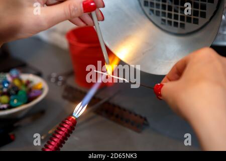 L'artiste chauffe le verre avec un brûleur à gaz. Le processus de fabrication de bijoux en verre. Les mains du maître se rapprochent Banque D'Images