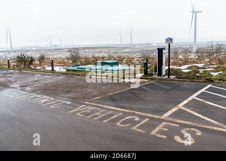 Station de charge pour les véhicules électriques avec éoliennes dans un champ enneigé en arrière-plan lors d'une journée d'hiver brumeuse. Concept d'énergie alternative. Banque D'Images