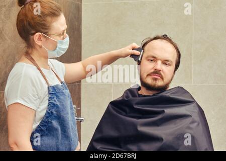 Une femme dans un tablier coupe les cheveux d'un homme avec une tondeuse Banque D'Images