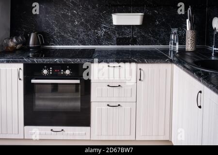 Cuisine en bois blanc avec comptoir et tablier noirs. Bouilloire, plaque de cuisson avec four Banque D'Images