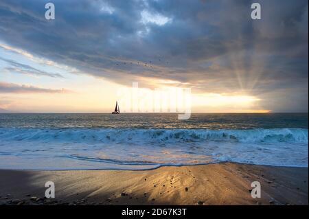 Un beau coucher de soleil avec un bateau naviguant le long de l'océan l'eau tandis que le soleil se rave à travers les nuages Banque D'Images