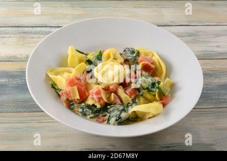 Tortellini au fromage aux épinards, cœurs d'artichaut et tomates en sauce crème dans un bol à soupe blanc sur la table Banque D'Images