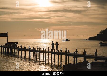 Le paysage de la silhouette du couple marchant sur le pont en bois au coucher du soleil sur l'île de Koh Kood, province de Trat, Thaïlande. Banque D'Images