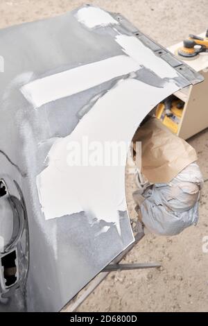 Réparation de la carrosserie, application PuTTY gros plan. Le mécanicien répare la voiture. Travailler après l'accident en travaillant le primaire de ponçage avant de peindre. Banque D'Images