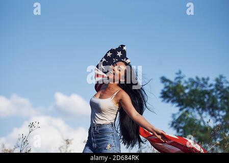 Femme patriote court avec le drapeau des Etats-Unis dans les mains à l'extérieur dans le champ contre le ciel bleu Banque D'Images