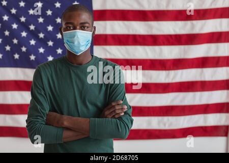 Portrait de l'homme afro-américain dans un masque protecteur debout avec son Bras croisés et regardant la caméra contre le drapeau américain Banque D'Images