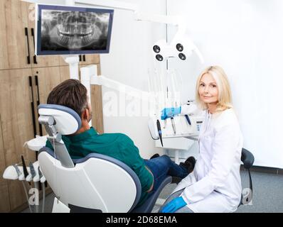 Portrait d'une femme dentiste souriant et regardant la caméra, sa patiente est assise à côté d'elle dans la chaise dentaire Banque D'Images