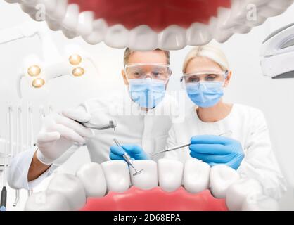 Dentiste et assistant avec perceuse dentaire et miroir dentaire, traitement des dents, concept de dentisterie créative. Vue depuis la bouche ouverte du patient Banque D'Images