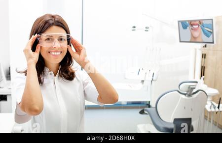 Portrait positif belle femme dentiste portant des lunettes de protection à la clinique dentaire moderne. Banque D'Images