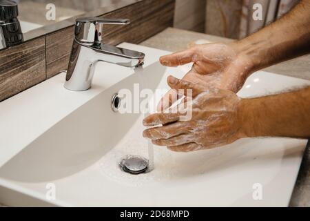 L'homme se lave les mains avec du savon pour prévenir le virus corona. L'eau s'écoule du mélangeur d'eau et un homme laque ses mains pour arrêter la propagation de Banque D'Images