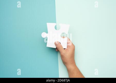 main mâle tenant de grands papiers blancs puzzles vierges sur un fond bleu, concept d'affaires Banque D'Images