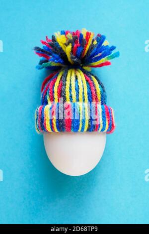 œuf blanc en laine tricotée chapeau coloré sur fond bleu, concept pâques, vue verticale du dessus Banque D'Images