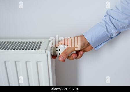 Main mâle Réglage du bouton du radiateur de chauffage. Une main qui régule la température dans le radiateur et les mains de la femme frottées avec le froid. Mains chaudes Banque D'Images