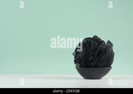 Accessoire de style noir pour le nettoyage de la peau - éponge de bain sur bol noir sur menthe verte menthe mur et table en bois blanc. Banque D'Images