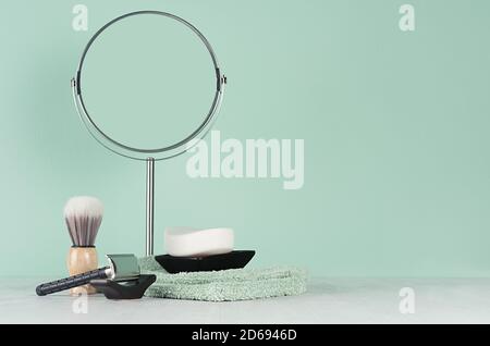 Intérieur de la salle de bain à la menthe menthe avec des accessoires pour le rasage en noir - rasoir, miroir rond, savon, serviette en coton, brosse à rasoir sur table en bois blanc. Banque D'Images