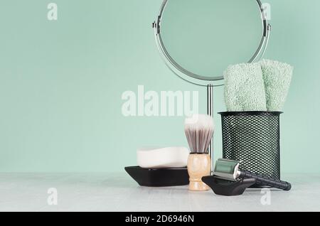 Produits de toilette noirs élégants pour le rasage - rasoir noir, savon, miroir rond, serviette, brosse de rasage sur planche en bois blanc et mur couleur menthe aqua, espace de copie, moi Banque D'Images