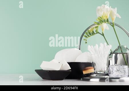 Mode noir cosmétiques accessoires en vert menthe l'intérieur de la salle de bains - miroir, tampons de coton, bourgeons, éponge, fleurs, brosse sur bois blanc. Banque D'Images