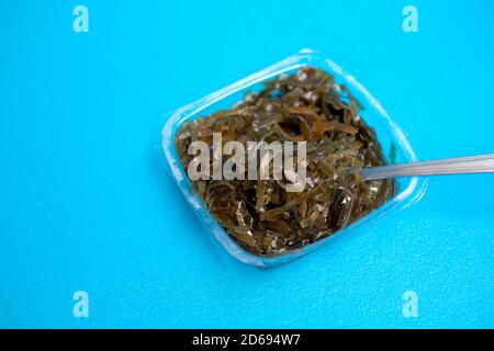 Une délicieuse salade d'algues fraîches. Salade d'algues comestibles et fourchette sur fond bleu. Banque D'Images