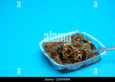 Une délicieuse salade d'algues fraîches. Salade d'algues comestibles et fourchette sur fond bleu. Banque D'Images