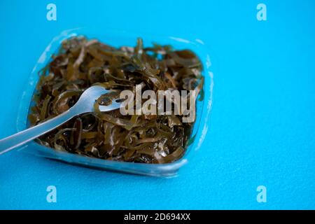 Une délicieuse salade d'algues fraîches. Salade d'algues comestibles et fourchette sur fond bleu. Banque D'Images