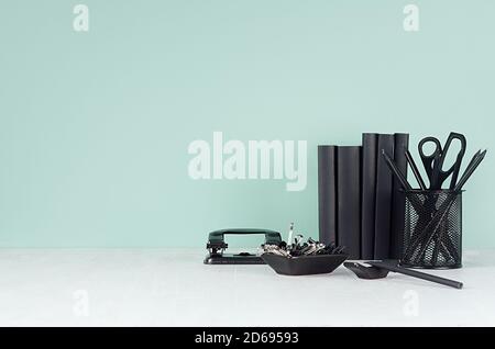 Lieu de travail élégant avec papeterie noire, livres, perforatrice sur la menthe verte menthe mur et table en bois blanc, espace de copie. Banque D'Images