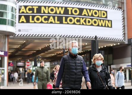 Les personnes qui portent un masque de visage marchent devant une publicité sur Market Street à Manchester, car la ville attend de savoir si la région sera placée dans la catégorie très haute avec des restrictions de niveau 3 de verrouillage pour freiner la propagation du coronavirus. Banque D'Images