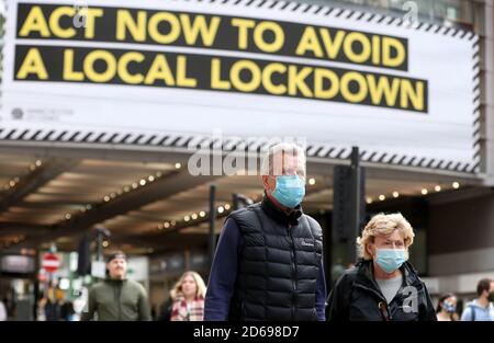 Les personnes qui portent un masque de visage marchent devant une publicité sur Market Street à Manchester, car la ville attend de savoir si la région sera placée dans la catégorie très haute avec des restrictions de niveau 3 de verrouillage pour freiner la propagation du coronavirus. Banque D'Images