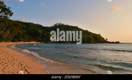 Plage tropicale Anse Takamaka dans le sud de Mahé, Seychelles avec sable, eau calme, palmiers, forêt tropicale et hébergement touristique en soirée. Banque D'Images