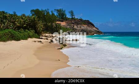 Plage tropicale Anse Capucins dans le sud de l'île de Mahé, Seychelles avec des empreintes de pas dans le sable, eaux turquoise et formations rocheuses de granit. Banque D'Images