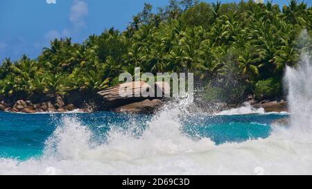 Mousse de puissantes vagues qui s'écrasent sur des rochers de granit sur la plage tropicale Anse Capucins, île de Mahé, Seychelles avec forêt tropicale en arrière-plan. Banque D'Images