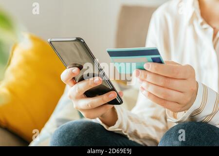 Photo d'une jeune femme méconnue qui fait ses achats en ligne avec le téléphone et une carte de crédit du canapé à la maison. Concept de commerce électronique Banque D'Images